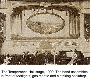 The Temperance Hall stage, 1909. The band assembles in front of footlights, gas mantle and a striking backdrop. 