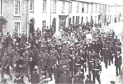The champions! The Rugby team of the 2nd battalion, the Welsh Regiment won the  the 1911-12 season cup. Here, complete with band, they carry the trophy shoulder high  down Laws Street.
